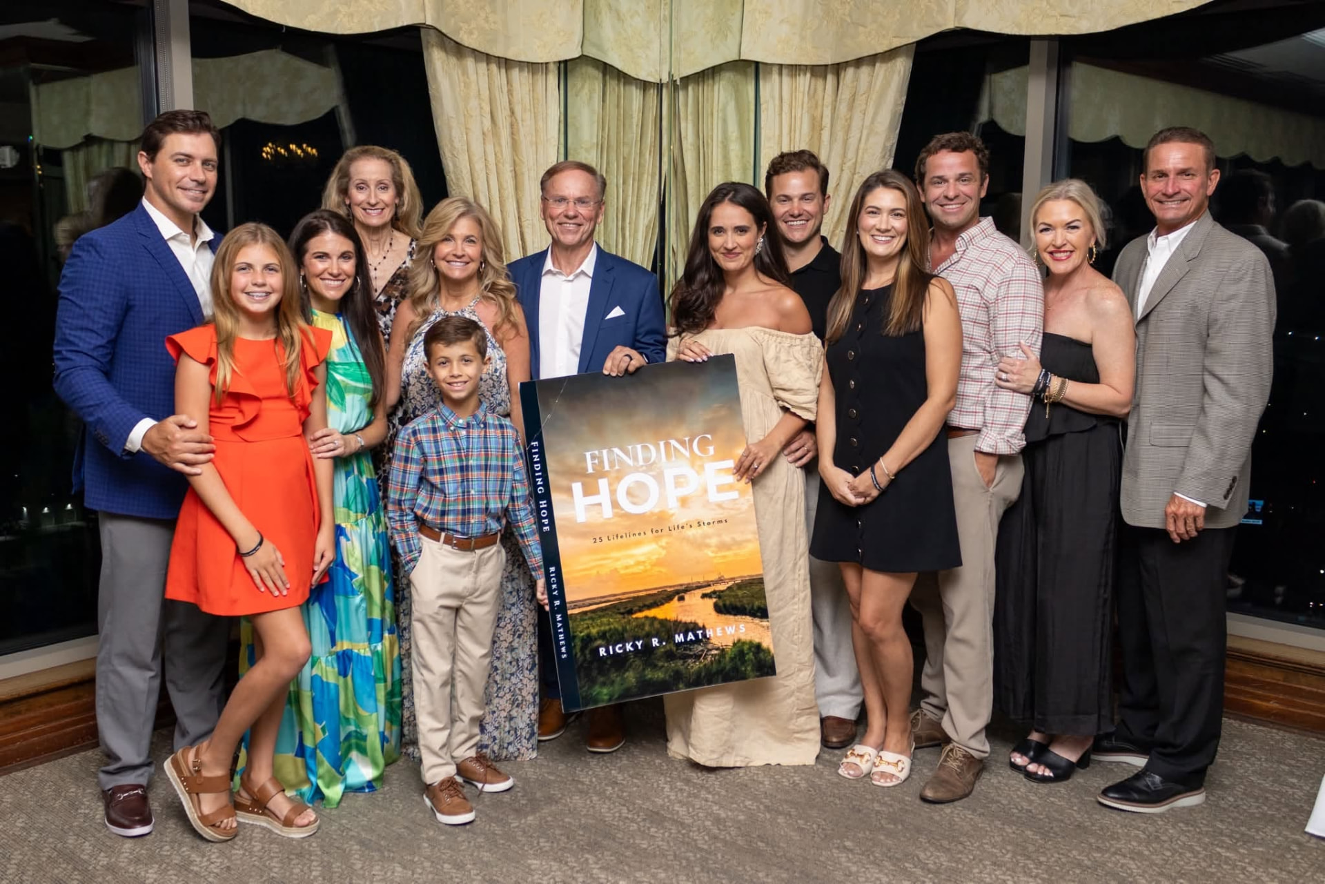 Ricky R. Mathews and family celebrating the Finding Hope book launch, holding a large framed cover of the book